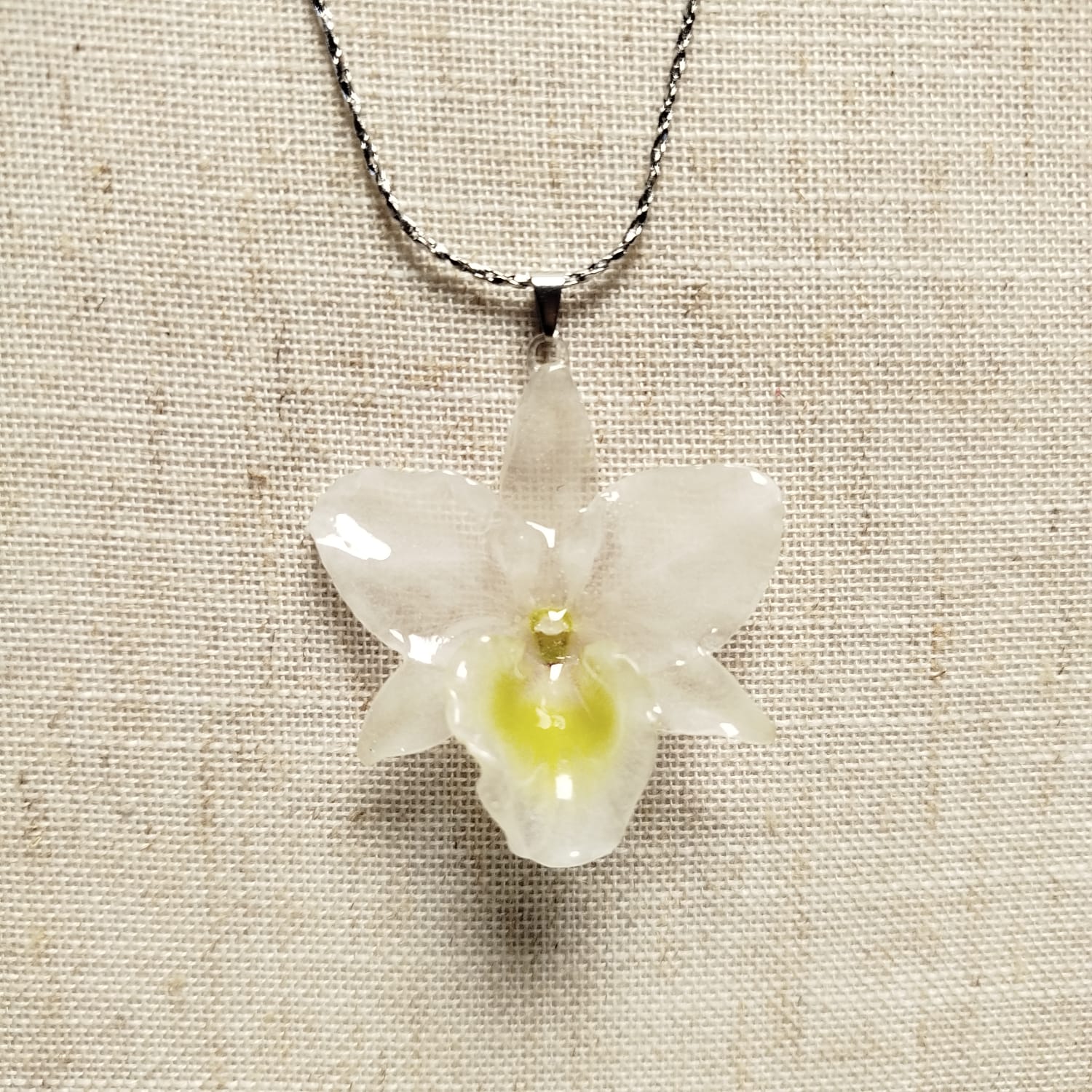 Colar com orquídea translúcida e centro amarelado sobre linho