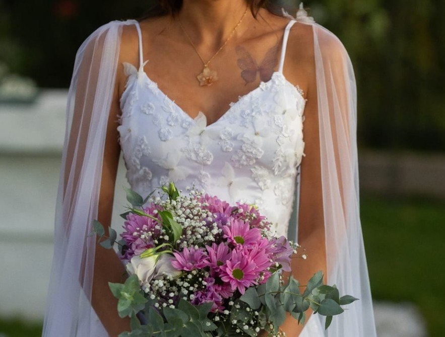 Noiva com vestido de renda segurando um buquê de flores rosadas e folhagens